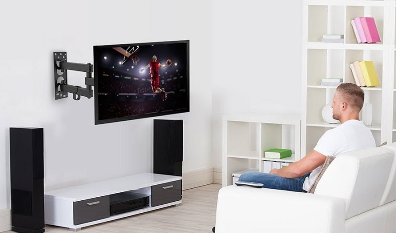 Người đàn ông đang xem tivi được lắp đặt bởi giá treo tivi đa năng gắn tường